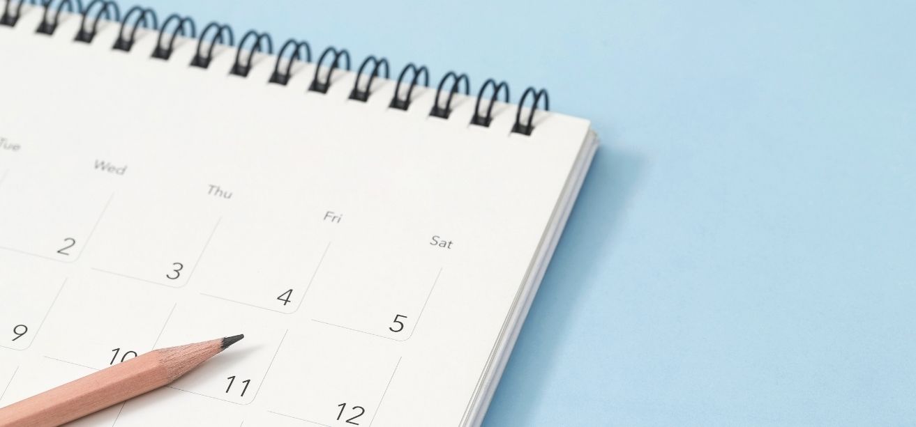Wooden pencil lying on an open desk calendar over a blue background.