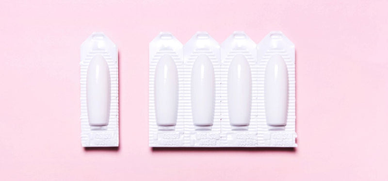 An image of a blister with suppositories on a pink background with one dose detached from the rest of the blister.