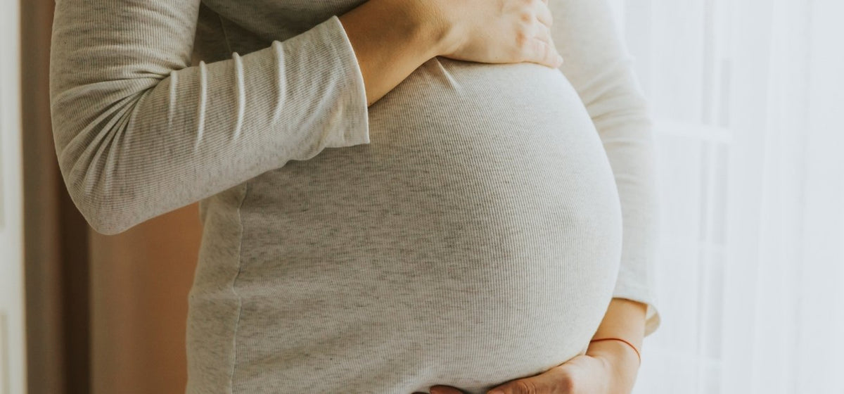 Close-up of a pregnant person cradling their baby bump over a white shirt.