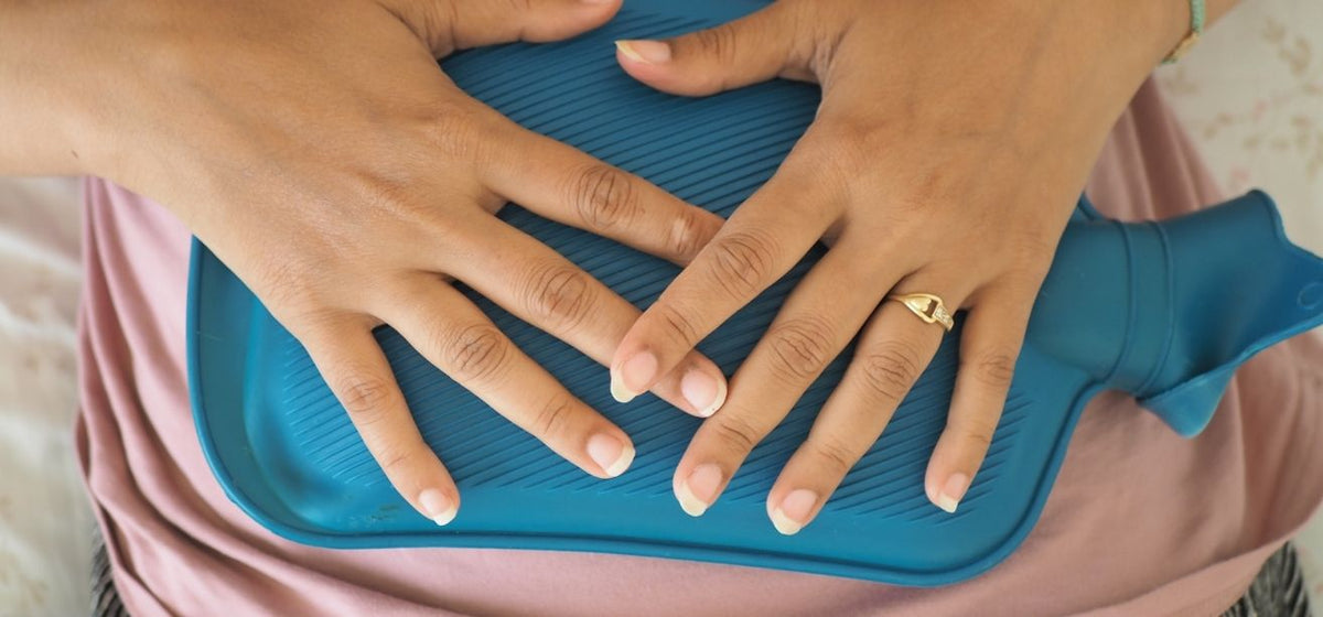 Woman holding a blue hot water bottle against her abdomen, illustrating cramping associated with bacterial vaginosis.