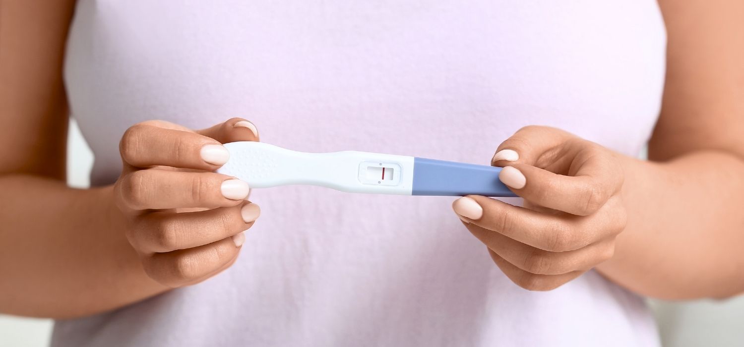 Close-up of a person's hands holding a pregnancy test showing a single red line, indicating a negative result.