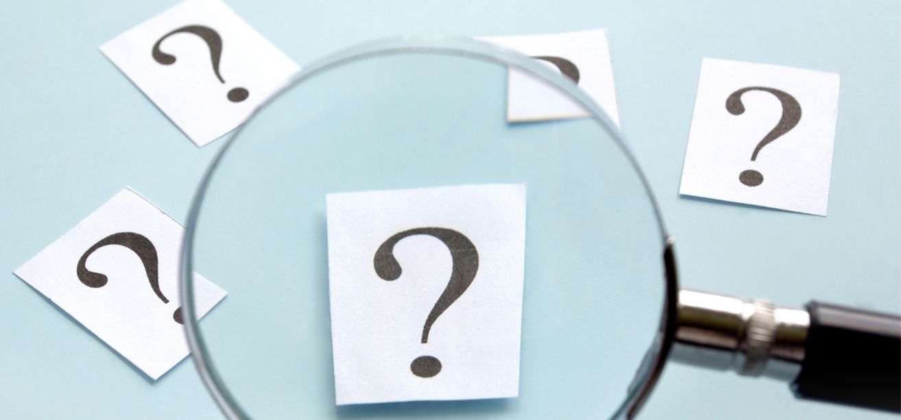 A magnifying glass held over paper slips printed with question marks.