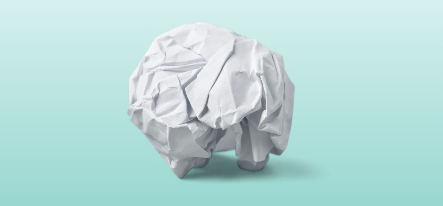 A crumpled ball of white paper shaped like a brain sits against a light teal background, symbolizing mental stress, tension, or cognitive overload.
