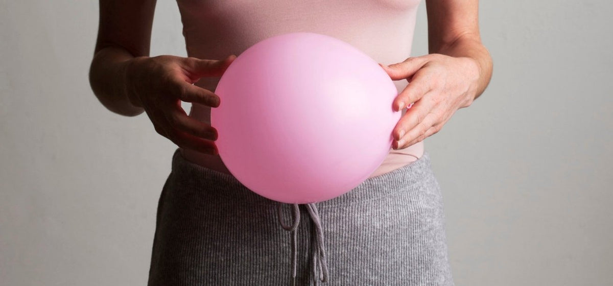 A close-up shot of a person holding a large, inflated pink balloon directly in front of their stomach.