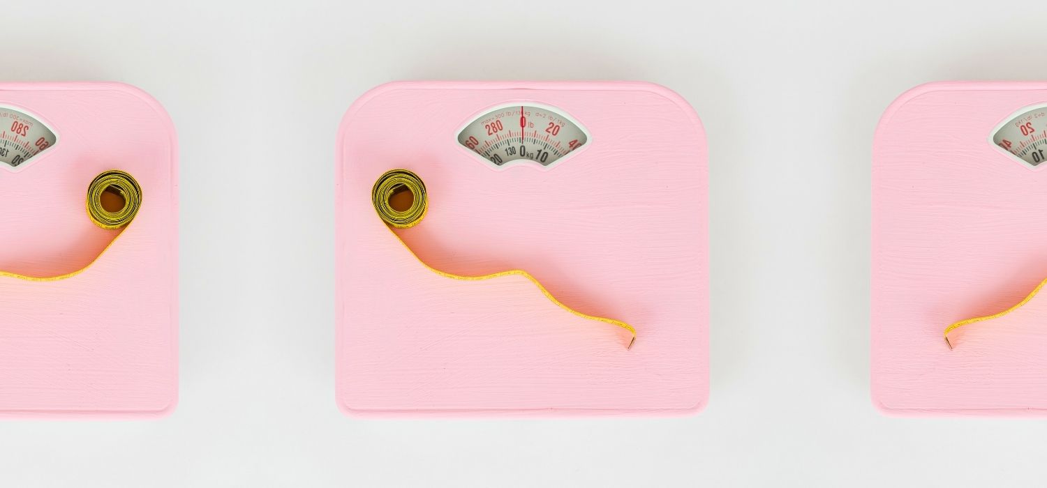 Three pink bathroom scales with yellow measuring tapes on a white background.