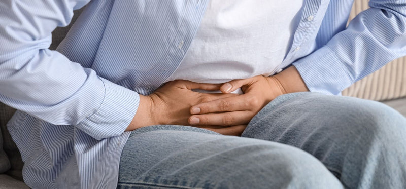A person holding their stomach in pain or discomfort while sitting on a couch.