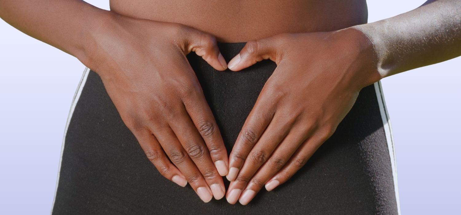 A close up image of a woman holding her hands in the shape of a heart in front of her pelvis.