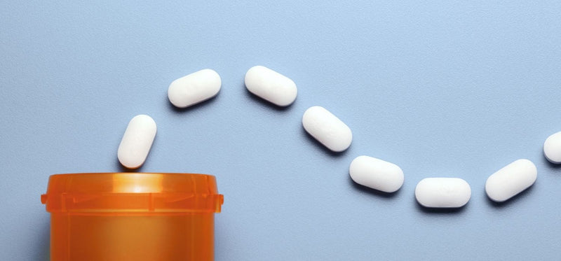 An open medicine container on a blue background with a line of pills coming out from the top.