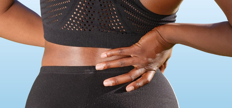 A close up of a woman holding her stomach with one pain, and supporting her back with the other hand.