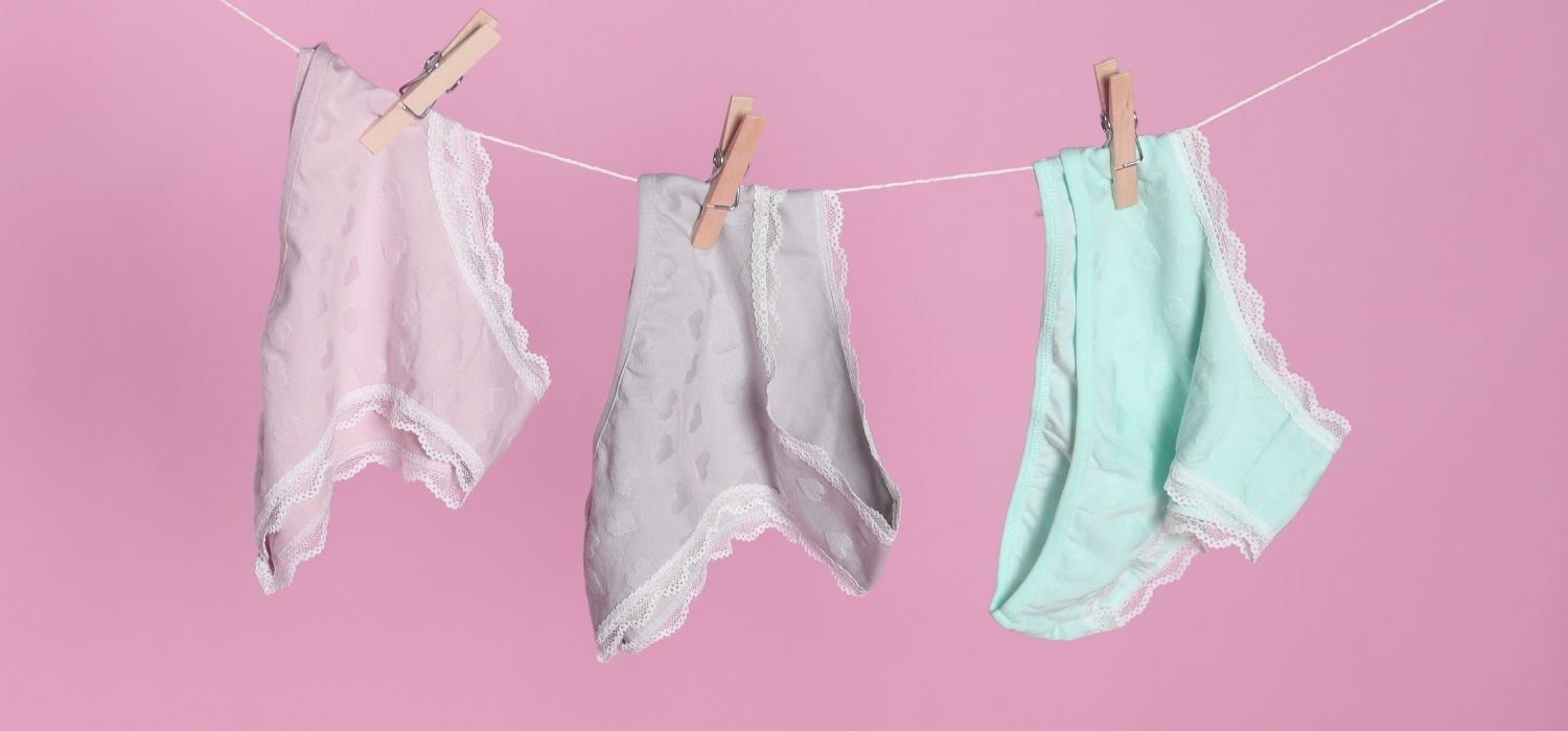 Three pairs of pastel-colored underwear hanging on a clothesline against a pink background.