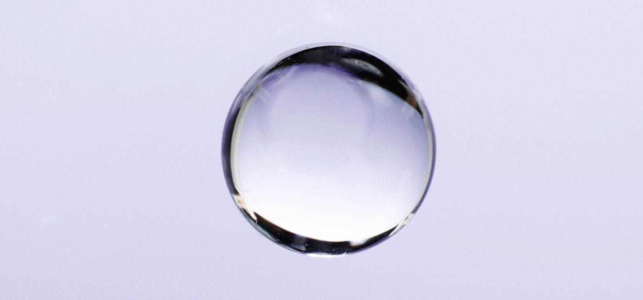 A single, water droplet centered on a light, pale purple background.