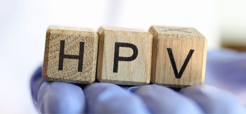 A person wearing blue medical gloves holding three wooden blocks that spell out "HPV."