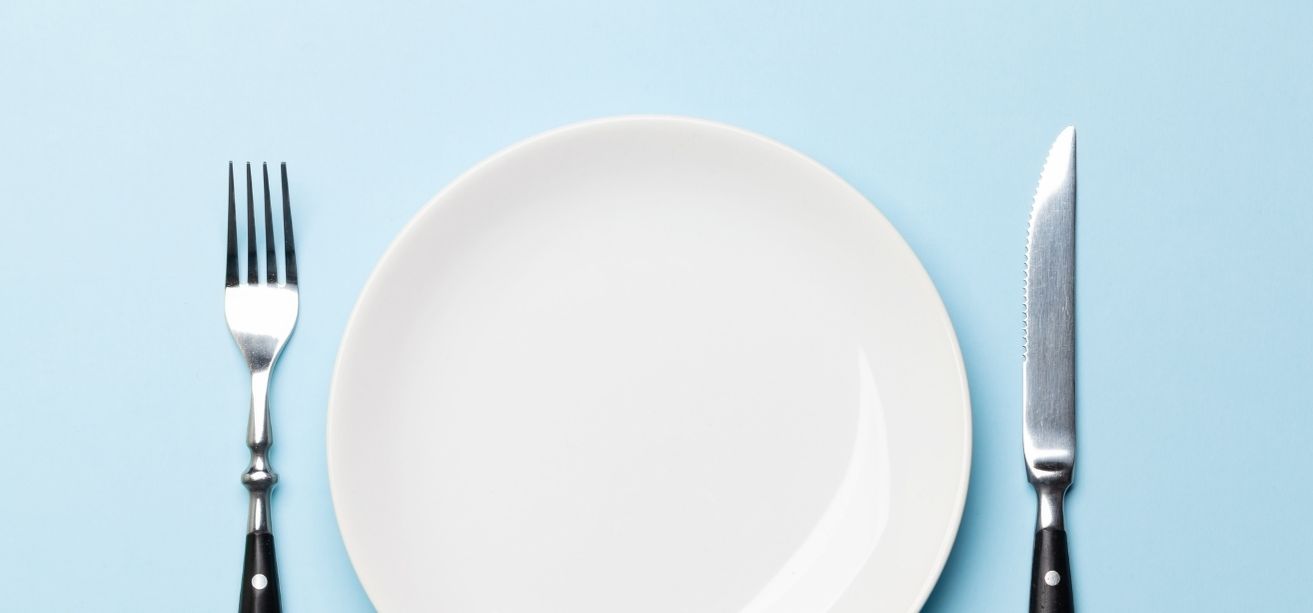 Empty white plate with a fork and knife on a blue background.