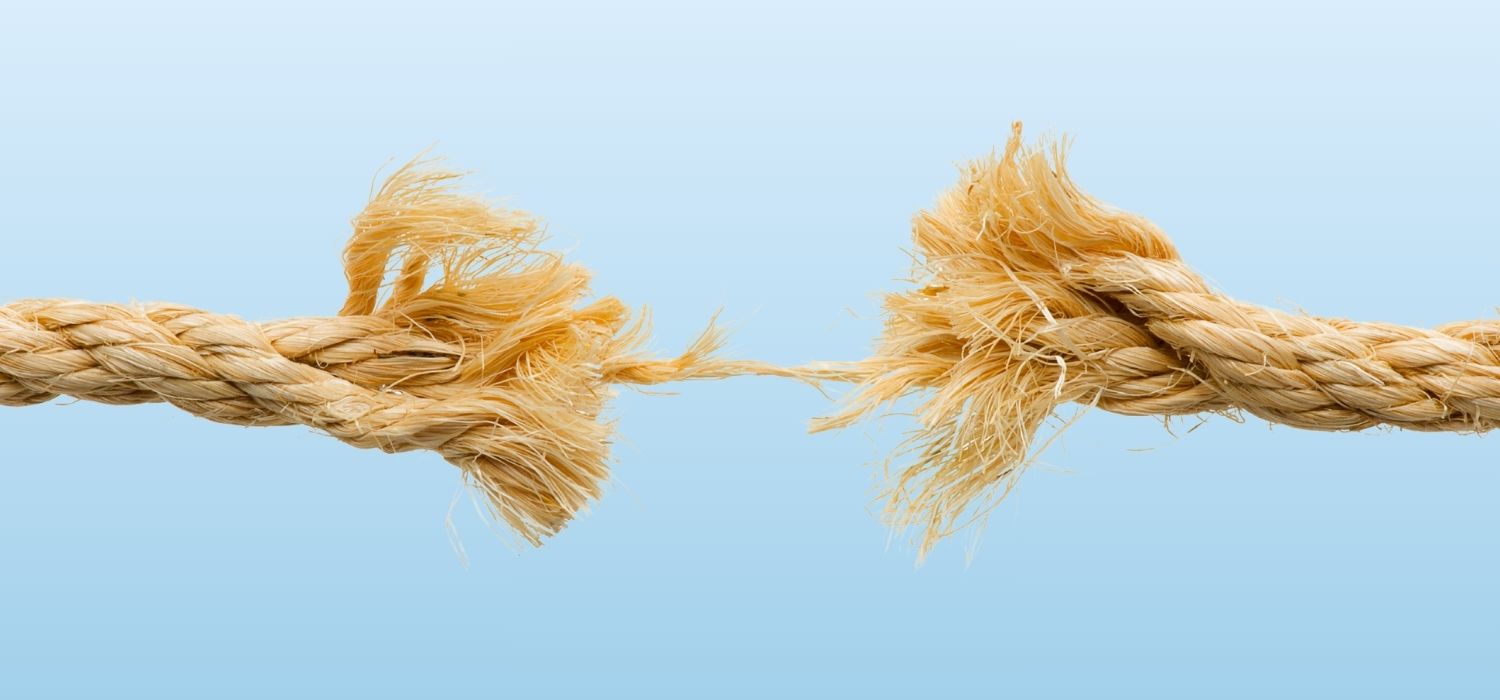A close-up of a thick, tan jute rope that is fraying and nearly snapped in the middle, held together by only a few thin strands against a light blue gradient background.