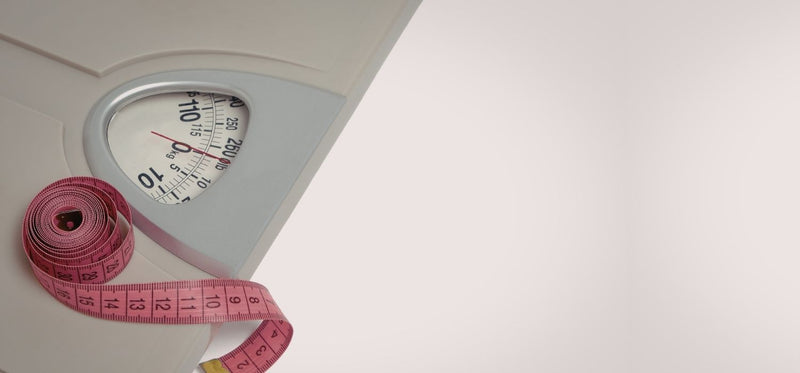 A bathroom scale and a pink measuring tape set against a clean, light background.