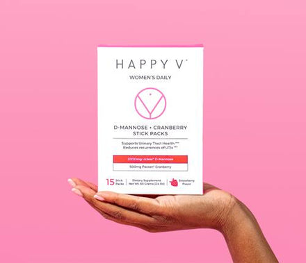 A woman's hand holding a box of Happy V's D-Mannose and Cranberry Stick Packs.
