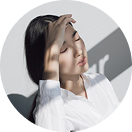 Woman in white shirt shielding eyes from sunlight, holding a Happy V supplement bottle.