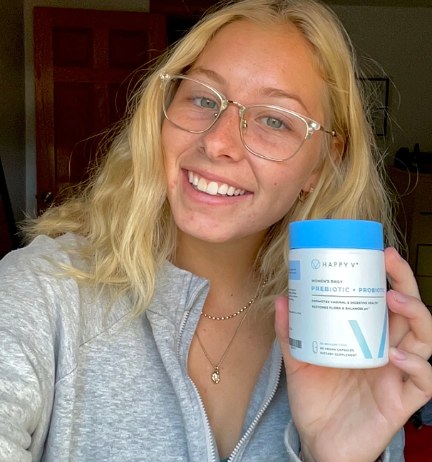 Young woman smiling and holding a container of Happy V prebiotic-probiotic supplement.