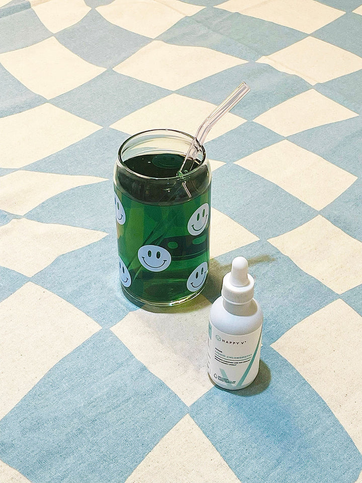 A Happy V glass filled with Happy V Liquid Chlorophyll next to a bottle of Happy V Liquid Chlorophyll bottle