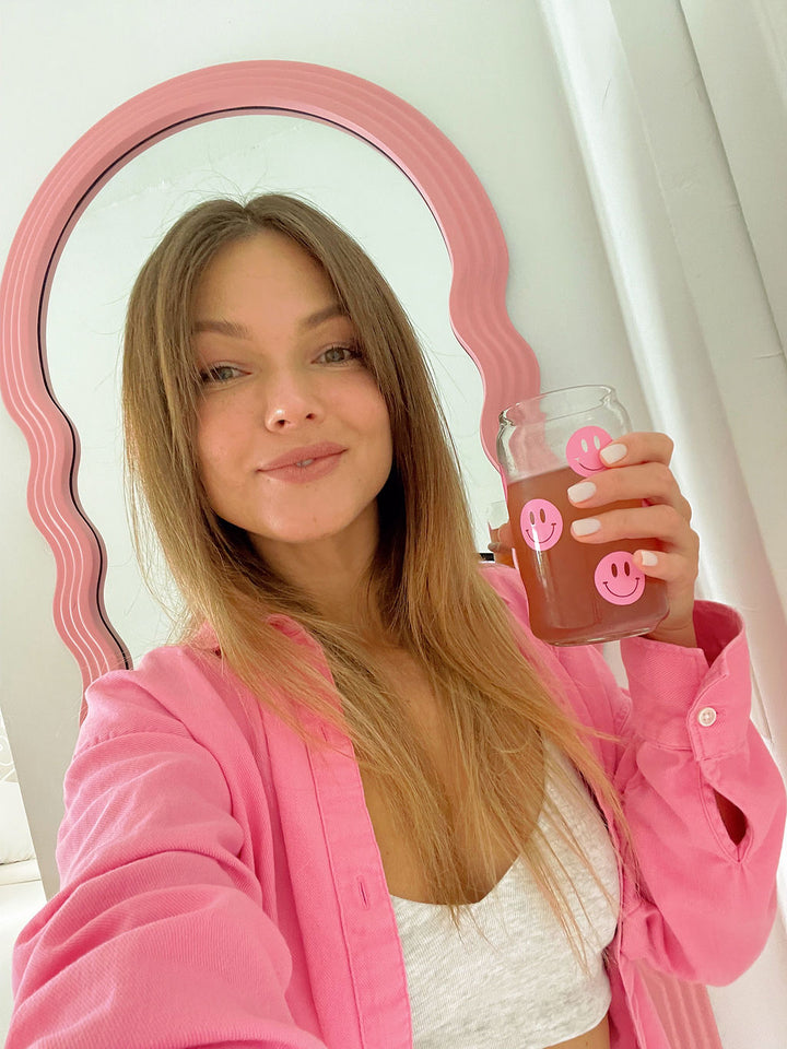 A smiling girl holding a Happy V glass full of Happy V D-mannose and Cranberry supplements next to her face
