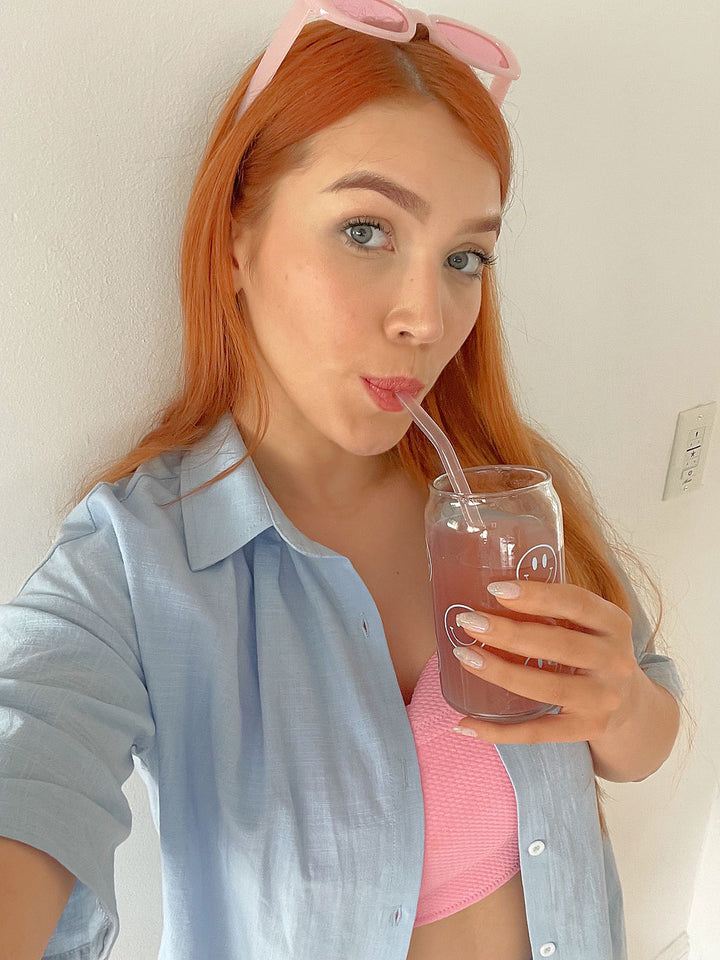 A girl with pink sunglasses drinking Happy V D-mannose and Cranberry Stick Pack from a Happy V glass
