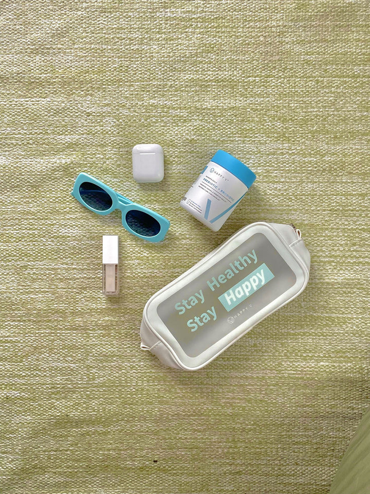 Happy V Prebiotic and Probiotic Supplements bottle laid next to an accessories bag, sunglasses, lipstick, and airpods