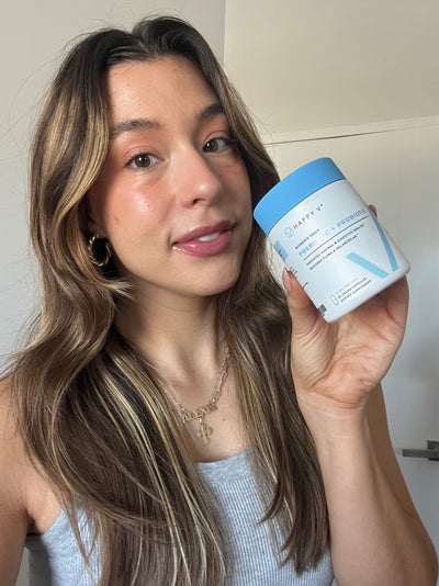 A smiling girl holding a bottle of Happy V Prebiotic and Probiotic Supplements.