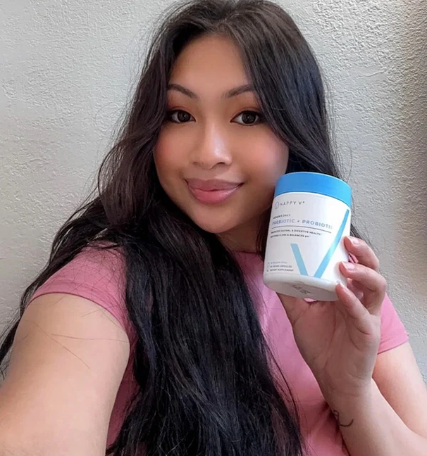 Woman holding a container of Happy V probiotic supplement in a bright setting.