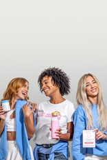 Three women smiling, holding Happy V supplement bottles, wearing casual outfits in a bright setting.
