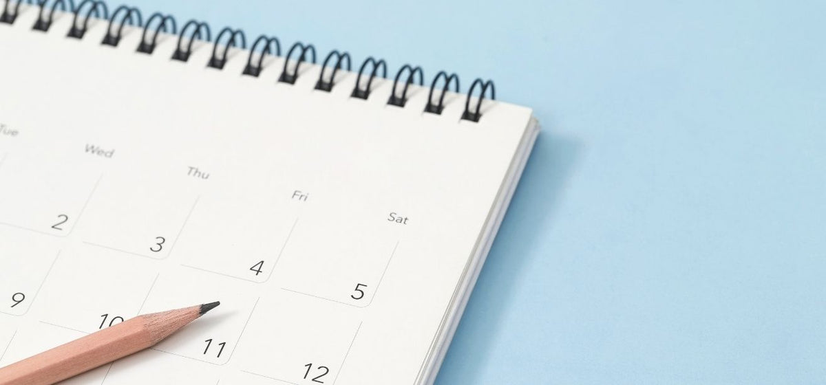 Wooden pencil lying on an open desk calendar over a blue background.