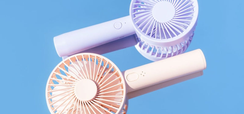 Two handheld portable fans in lavender and cream on blue background, illustrating cooling relief for hot flashes or temperature regulation.