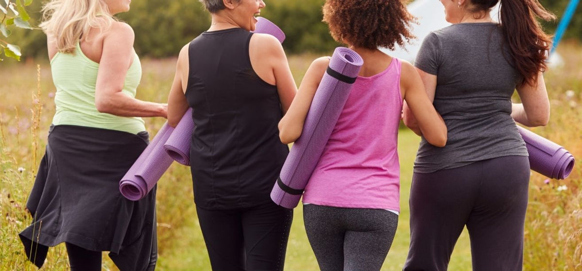 Group of women jogging together outdoors carrying yoga mats in athletic wear.