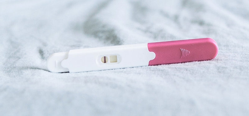 A negative pregnancy test stick with a pink cap lying on a soft grey blanket.