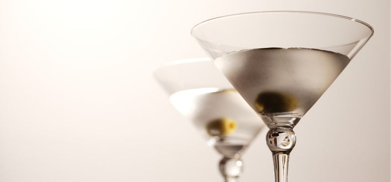 Two martini glasses with olives against a neutral background.