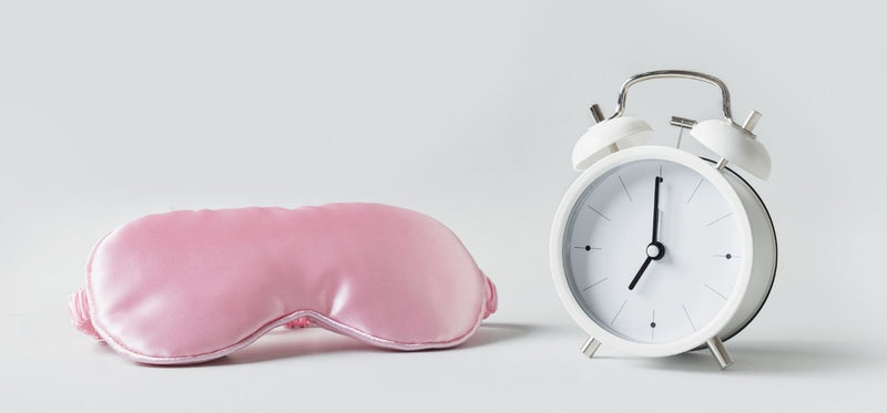 A pink sleep mask and a white alarm clock on a plain gray background.