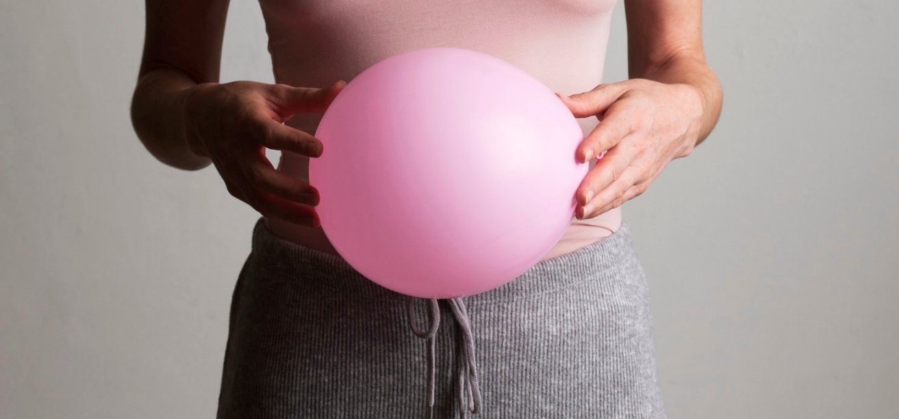 A close-up shot of a person holding a large, inflated pink balloon directly in front of their stomach.