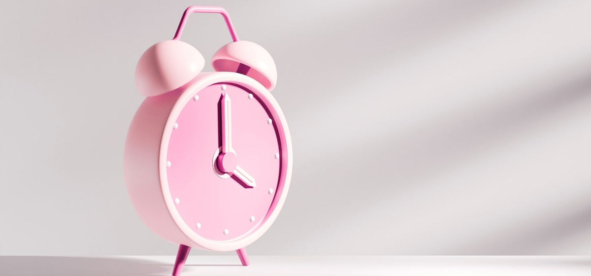 A close up of a pink alarm clock on a grayish background.