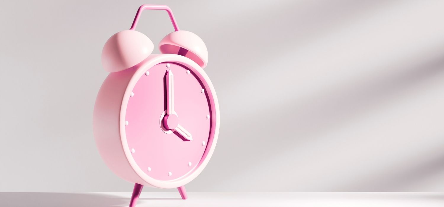 A close up of a pink alarm clock on a grayish background.