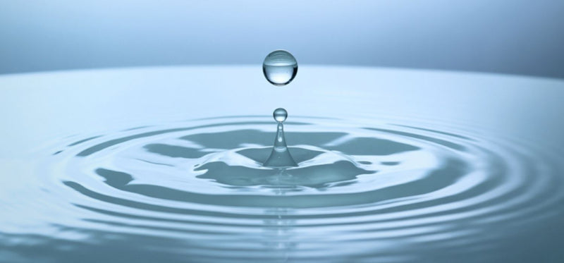 A close up of a water droplet falling into a pool of water.