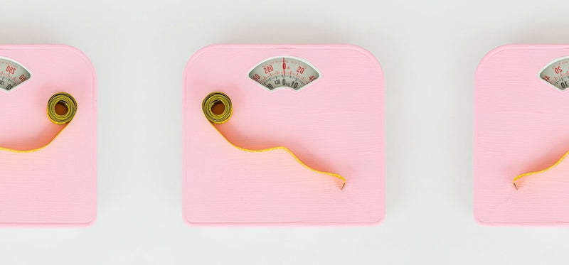 Three pink bathroom scales with yellow measuring tapes on a white background.
