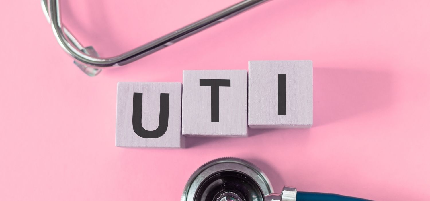 An image of letter cubes, spelling out the word UTI, surround ed by a stethoscope, against a pink background.