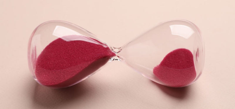Hourglass lying on its side with pink sand on a beige background.
