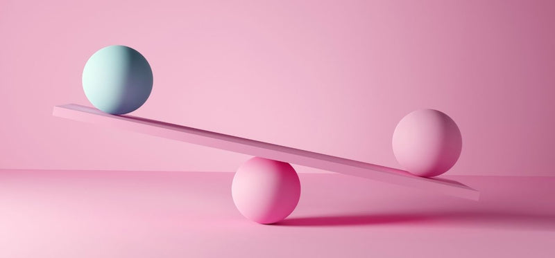 Unbalanced seesaw with a teal sphere and a pink sphere on a pink background, illustrating hormonal imbalance in women.