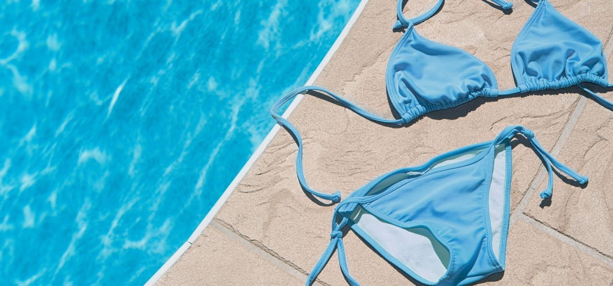 Blue bikini laid out on the tiled edge of a swimming pool.