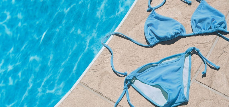 Blue bikini laid out on the tiled edge of a swimming pool.