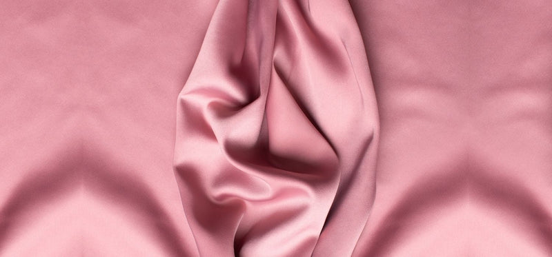 Close-up of draped pink silk fabric with artistic folds and a soft, lustrous texture.