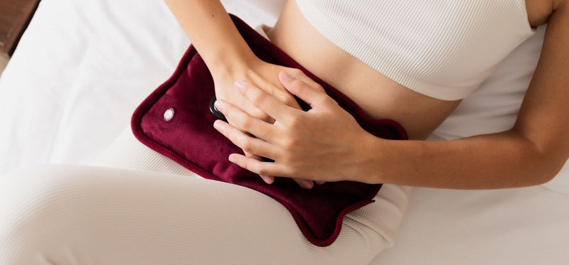 A person using a red hot water bottle on their stomach for comfort.