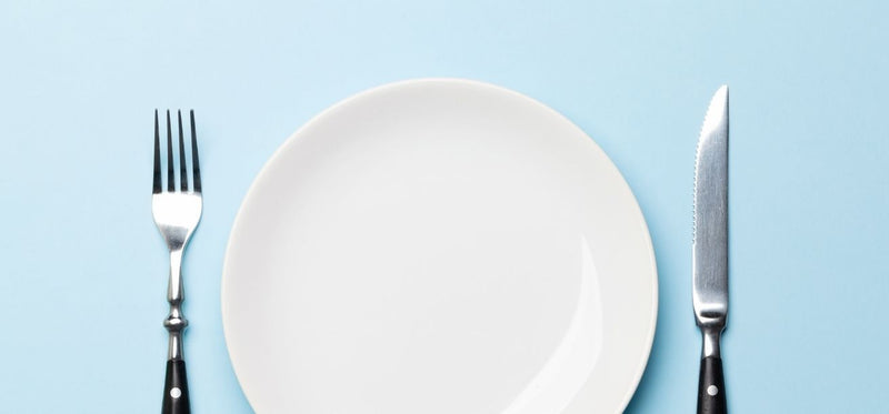Empty white plate with a fork and knife on a blue background.