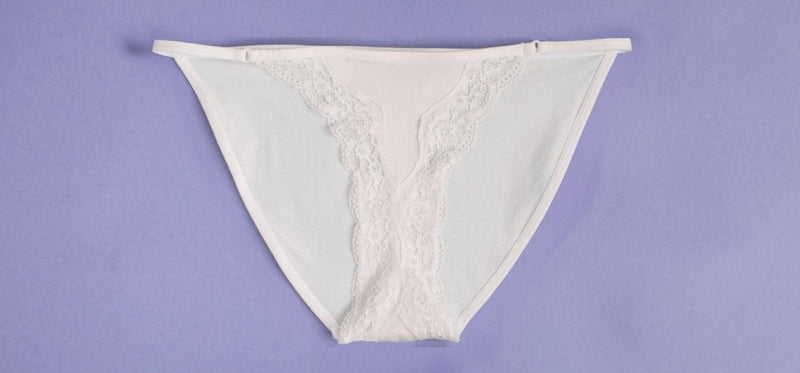 White lace-trimmed underwear laid flat on a solid purple background.