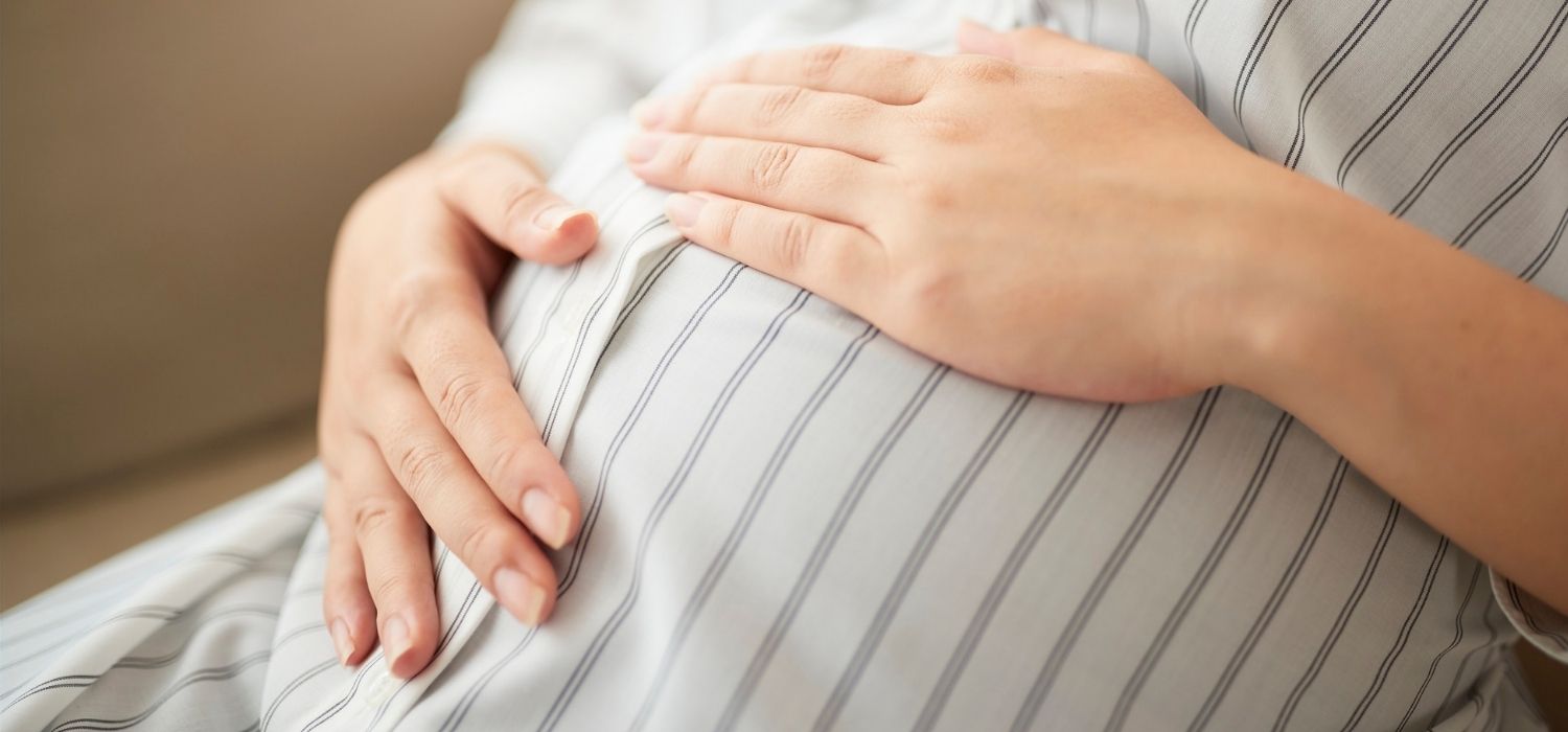 A close up image of a pregnant woman in a pajama, holding her belly.